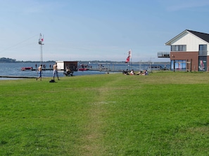 A grassy area with a dock and a building with a balcony overlooking a body of water. - Exclusive Apartment on the Ground Floor Directly Located on the Water (Kamperland)
