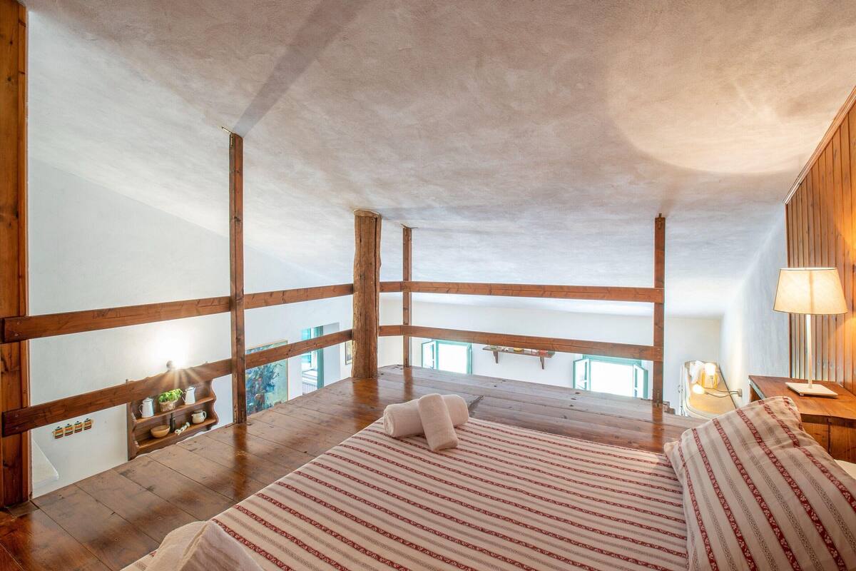 Une chambre avec un plafond en bois, un grand lit avec une literie à rayures et une vue sur l’extérieur.