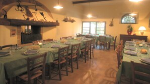 A dining area with multiple tables set for meals, wooden chairs, and a brick fireplace. - Appealing Apartment in Collesalvetti With Garden (Collesalvetti)