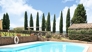 A swimming pool with a clear blue water, surrounded by a brick wall and metal railing. Tall trees and a tiled roof structure are visible in the background. - Appealing Apartment in Collesalvetti With Garden (Collesalvetti)