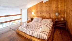 A wooden-paneled bedroom with a bed, two bedside tables, and a nightstand. - Appealing Apartment in Collesalvetti With Garden (Collesalvetti)