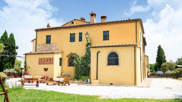 A two-story building with a yellow facade, a small garden with outdoor seating, and a clear blue sky. - Appealing Apartment in Collesalvetti With Garden (Collesalvetti)