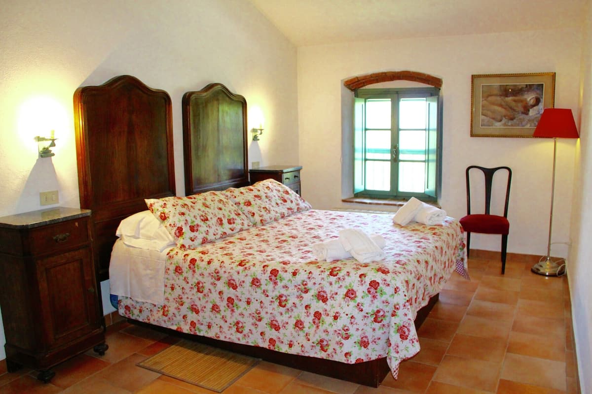 Une chambre à coucher avec un lit double, une tête de lit en bois, des tables de chevet, une fenêtre avec vue, un fauteuil rouge et une lampe.