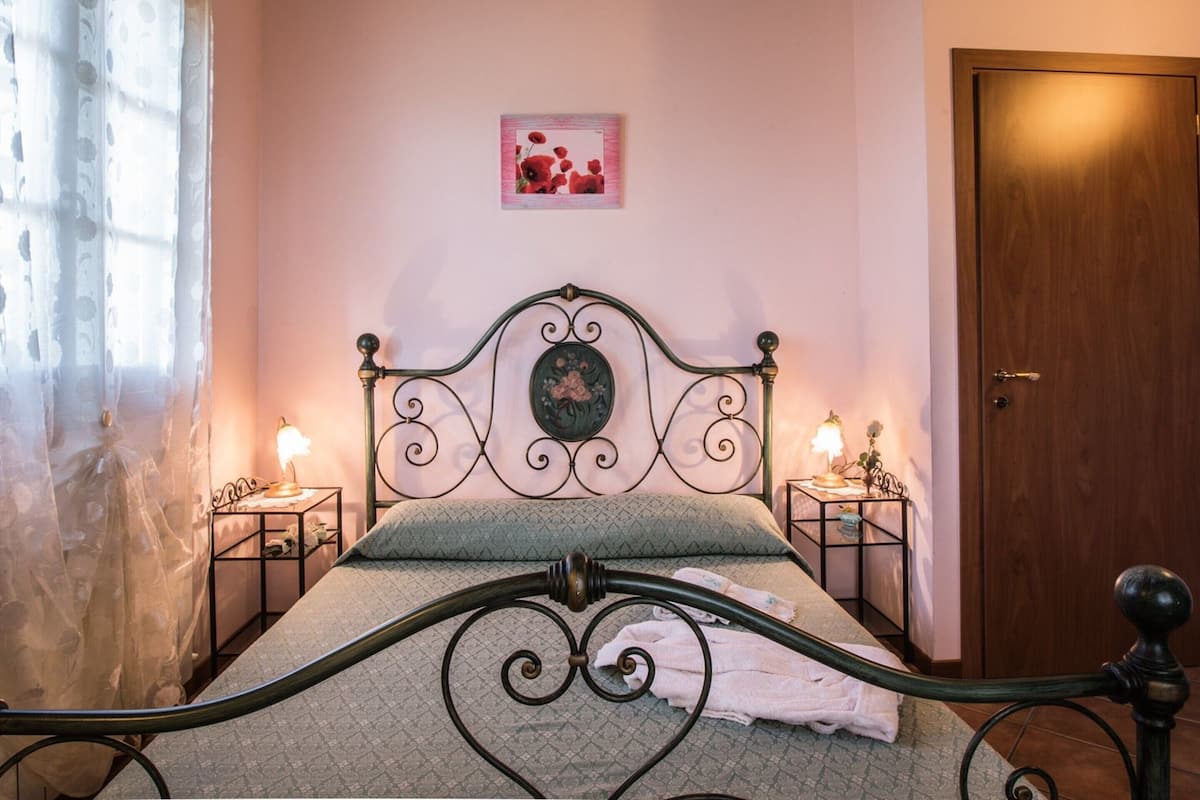 A bedroom with a bed, two bedside tables, a wooden door, and a wall-mounted picture.