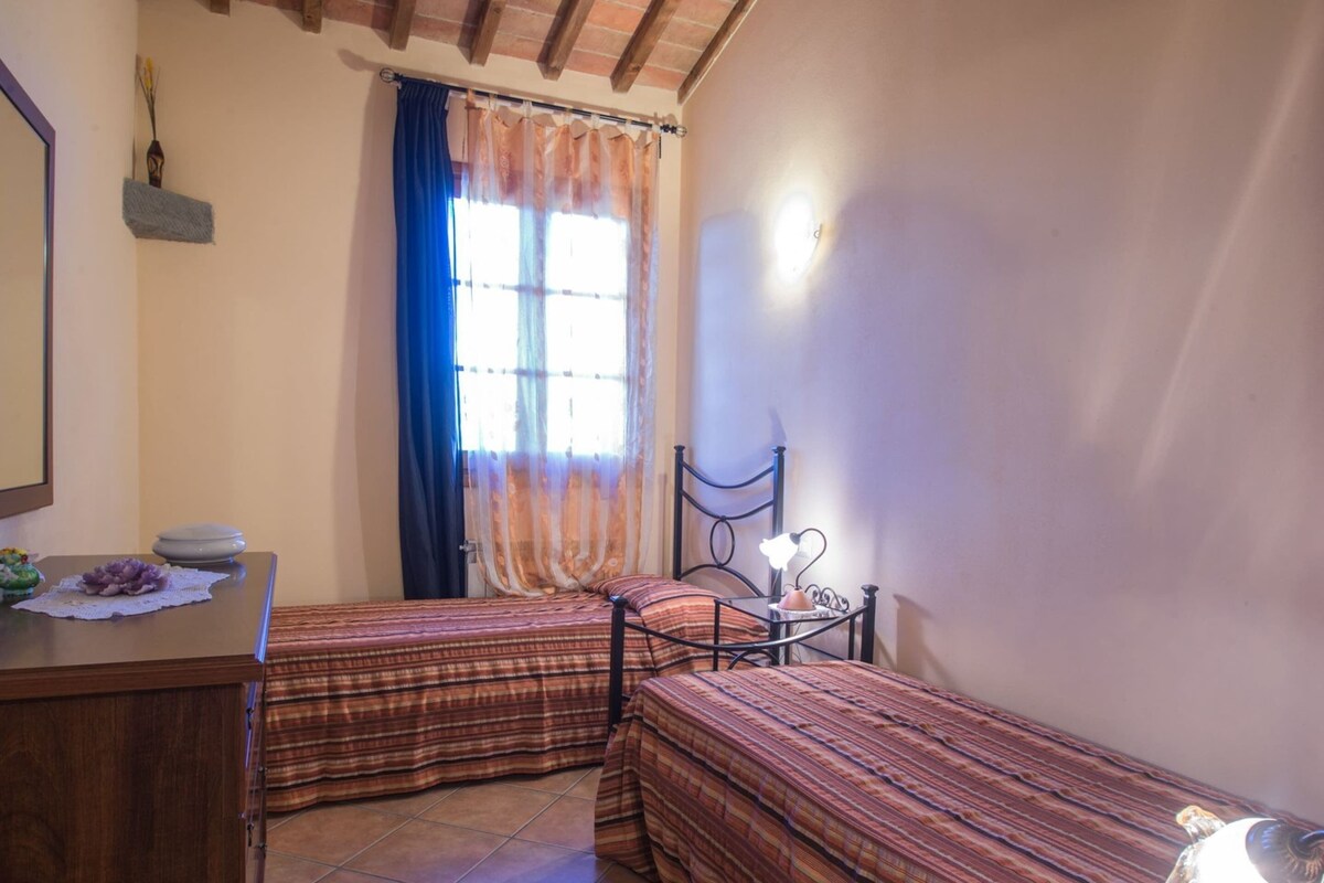 A bedroom with two beds, a wooden dresser, a nightstand, and a window with curtains.