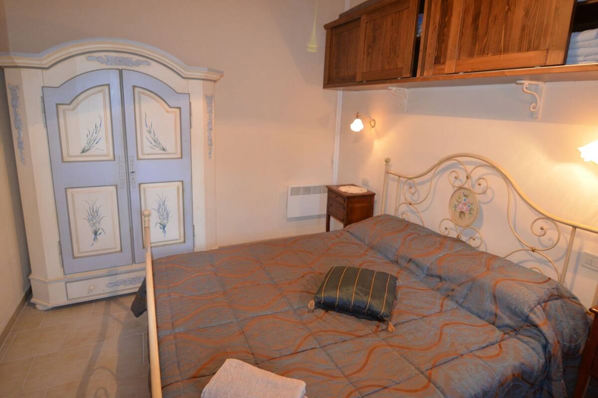 Quarto com cama, guarda-roupa, mesa de cabeceira e prateleira na parede.