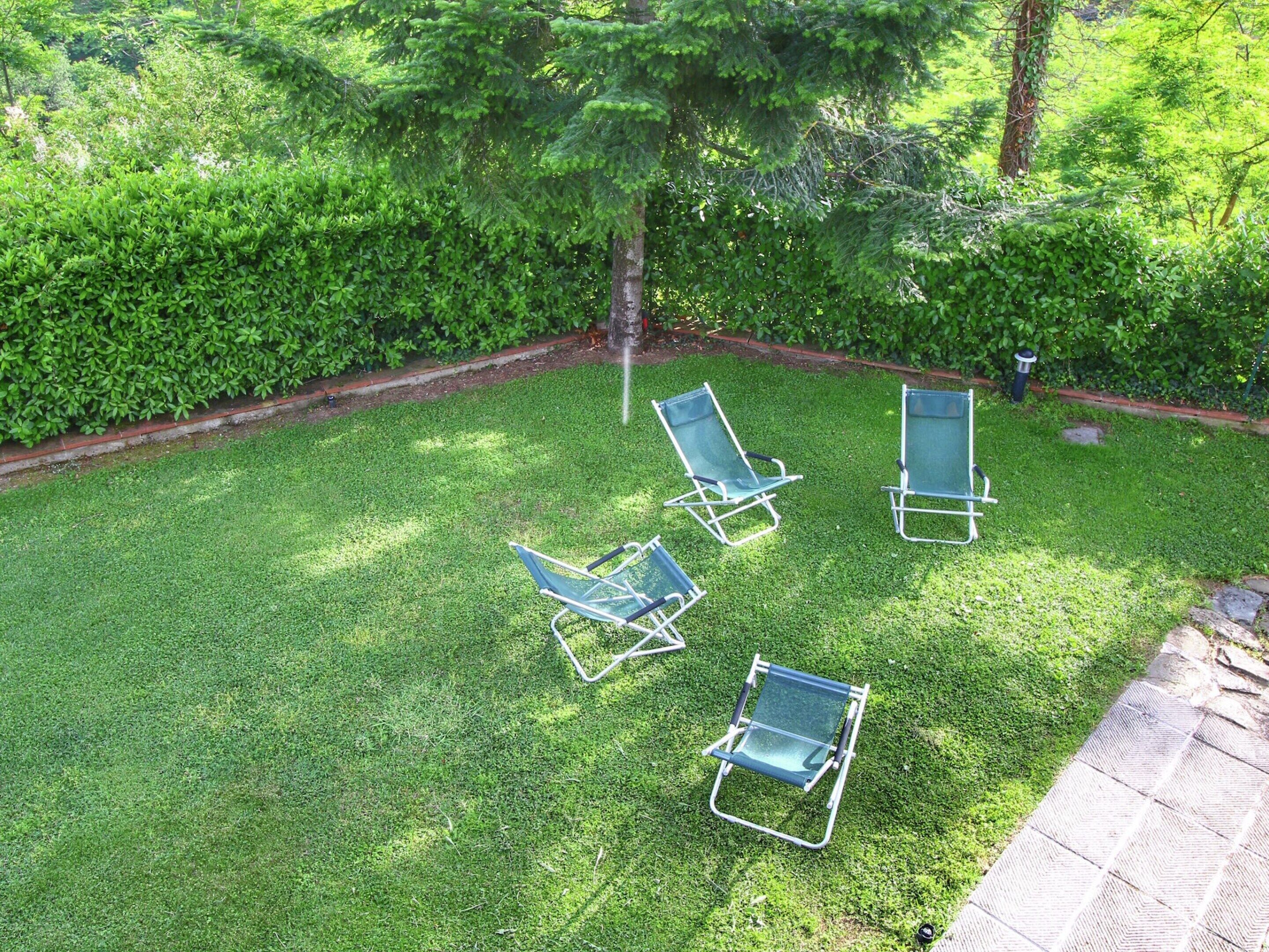 A well-maintained lawn with four green lawn chairs arranged in a semi-circle.