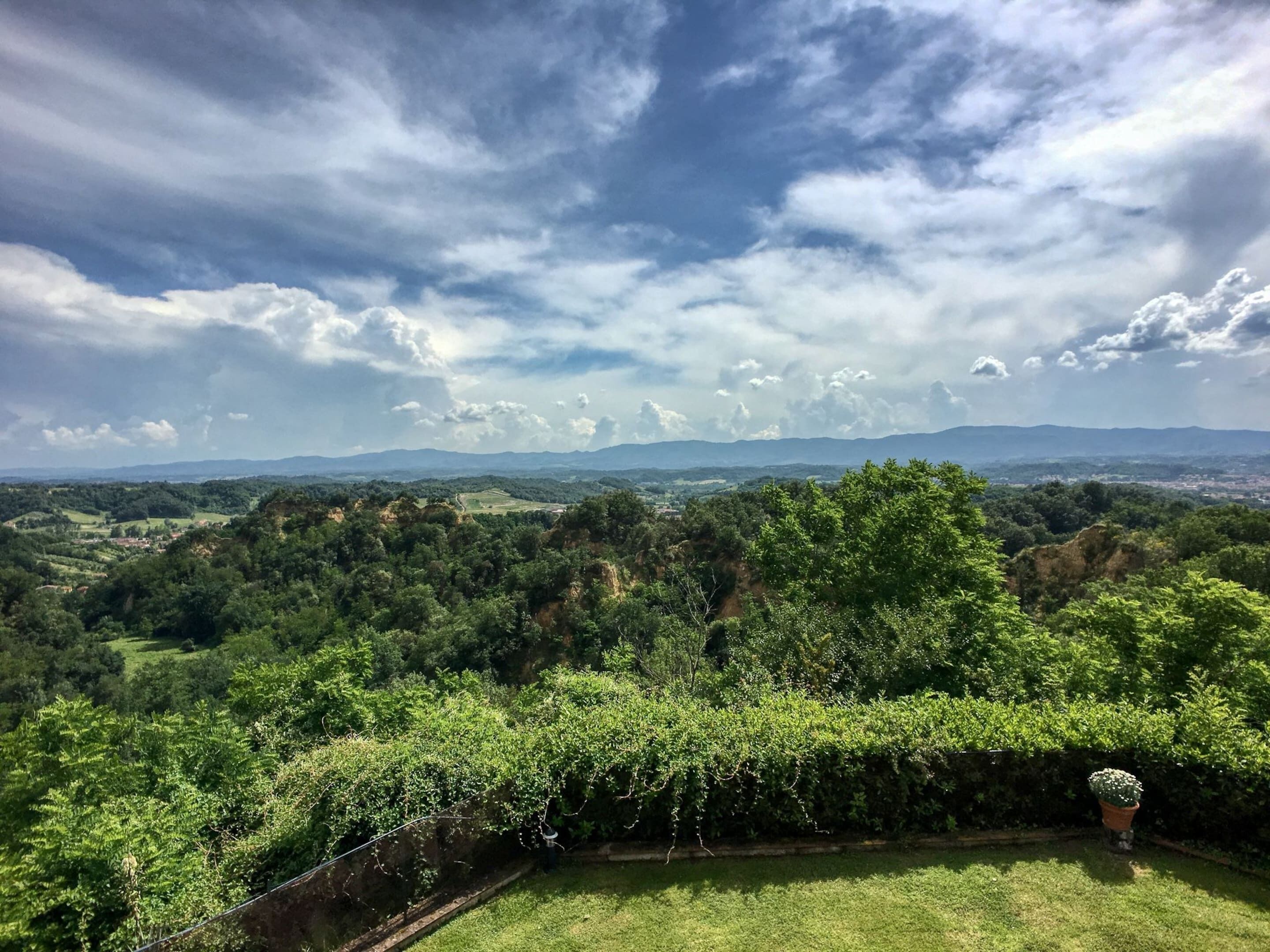 Una vista panorámica de un paisaje exuberante con colinas ondulantes y una cadena montañosa distante bajo un cielo parcialmente nublado.