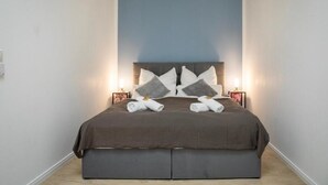A neatly made bed with a dark brown bedspread, two pillows, and two rolled towels. - HANNIBAL - Design Apartment Lilie 2 (Wolfsburg)