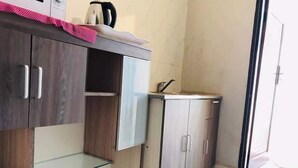 A kitchen with wooden cabinets, a glass shelf, and a small countertop. - T3C GARDENS (Lusaka)