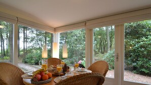 A breakfast table with wicker chairs, a basket of fruit, and a glass of orange juice. - A Detached Bungalow With Outdoor Fireplace, Covered Terrace and Pond in a Forest Plot (Wateren)