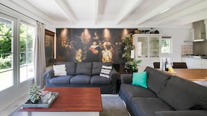 A modern living room with a dark grey sofa, a wooden coffee table, and a large painting on the wall. - A Detached Bungalow With Outdoor Fireplace, Covered Terrace and Pond in a Forest Plot (Wateren)