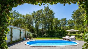 A rectangular swimming pool with a paved deck, surrounded by lush greenery and trees. - A Detached Bungalow With Outdoor Fireplace, Covered Terrace and Pond in a Forest Plot (Wateren)