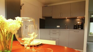 Een moderne keuken met grijze kastjes, een koffiezetapparaat en een eettafel gedekt met een bloevas, wijnglazen en borden.