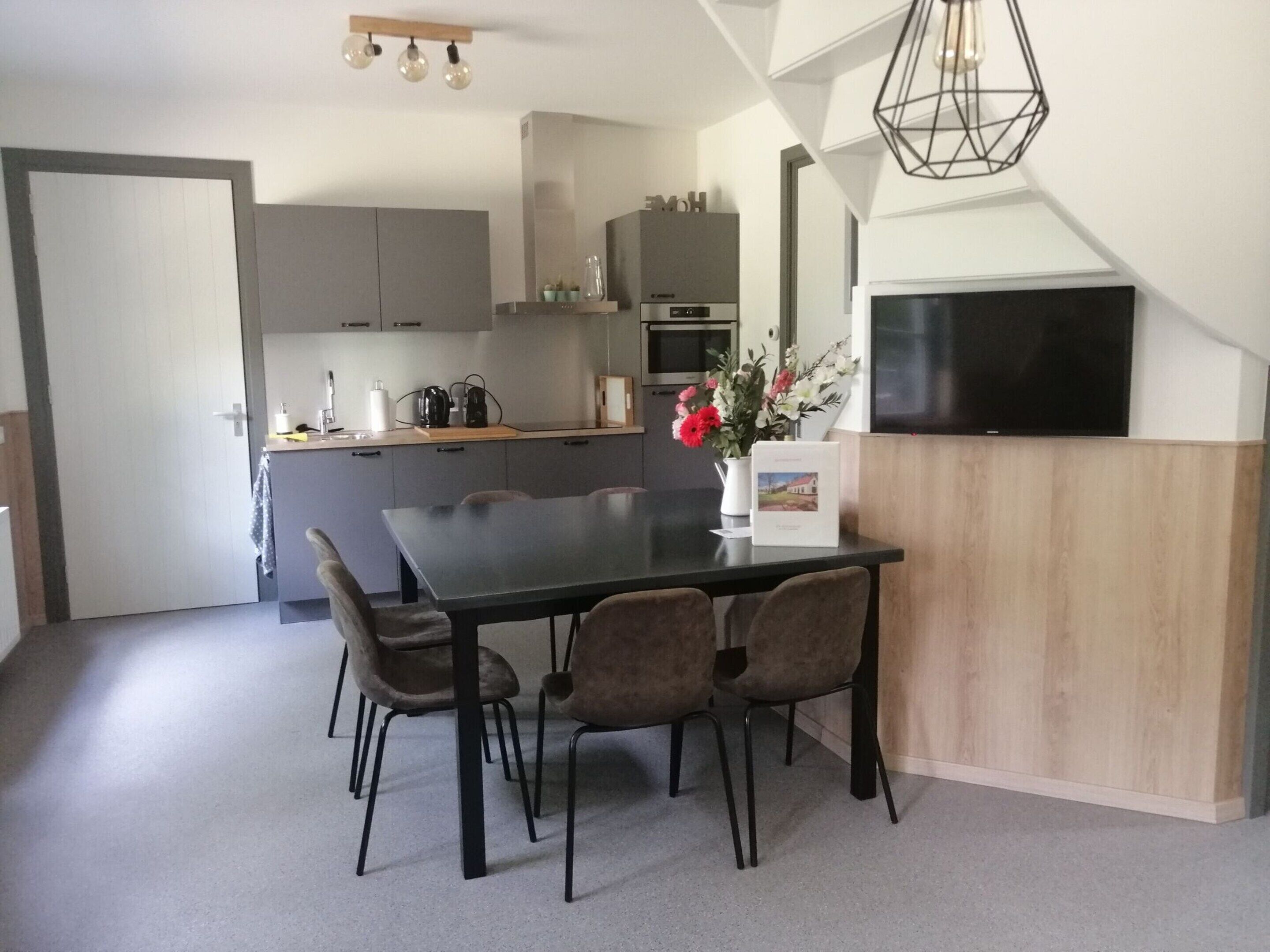 Uma cozinha moderna com armários cinza, uma mesa de jantar de madeira e uma TV preta fixada na parede.