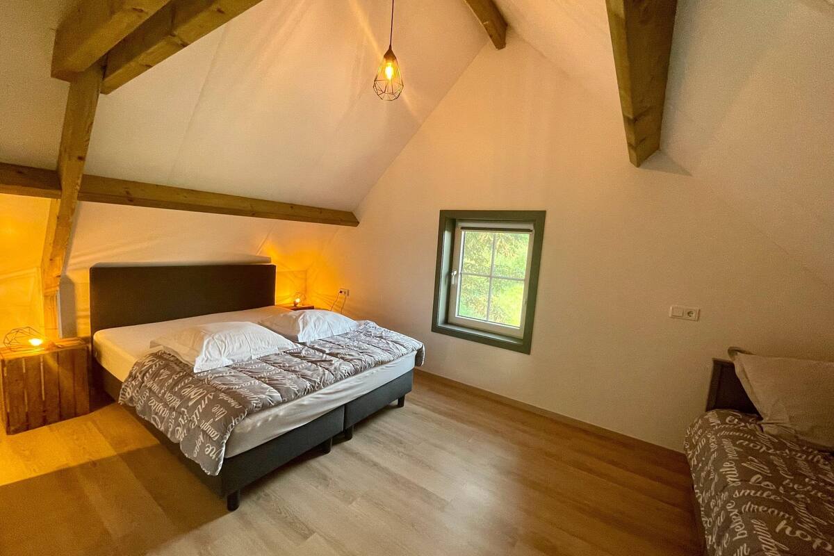 A bedroom with a bed, wooden beams, a window, and a hanging light fixture.