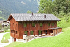 A wooden chalet with a sloped roof, large windows, and a stone staircase leading to a patio area. - Grand Apartment in Mayrhofen With Infrared Sauna & Artistic Interiors (Ramsau im Zillertal)