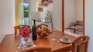 A dining area with a wooden table set for two, a bowl of fruit, a bottle of wine, and a vase of flowers. - Panoramic Apartment in Banjole Near Pula Town Centre (Medulin)