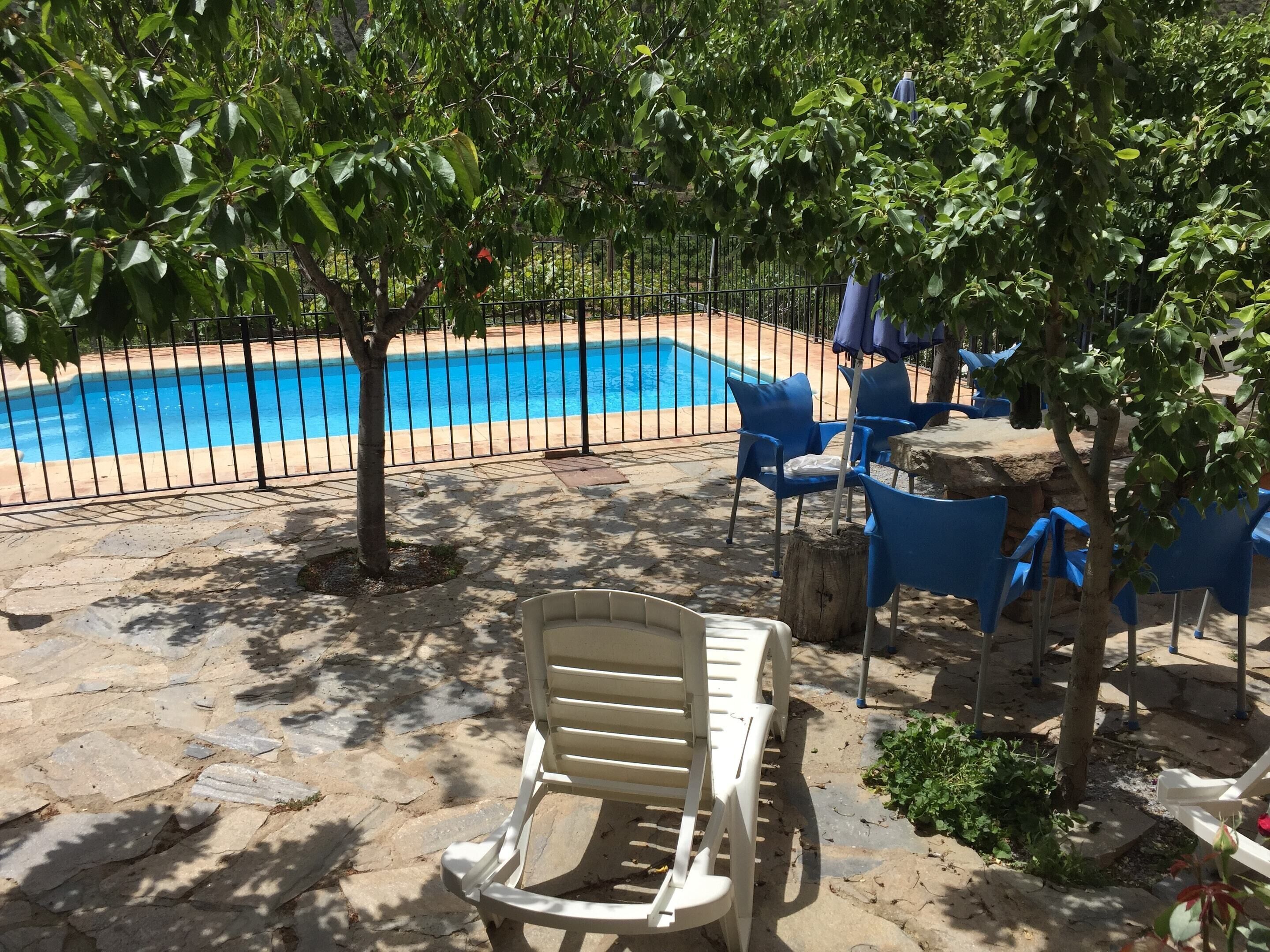 A pool area with a stone patio, blue chairs, and a white lounge chair.