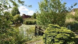 A serene garden with a pond, surrounded by lush greenery and a wooden bridge. - Cozy Apartment in Rerik Near the Beach (Rerik)
