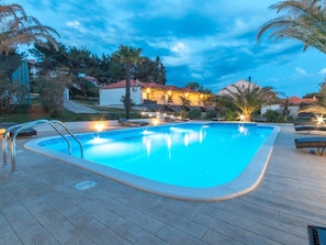 A swimming pool with a wooden deck, surrounded by palm trees and houses. - Scenic Holiday Home in Bibinje Near Sea (Bibinje)