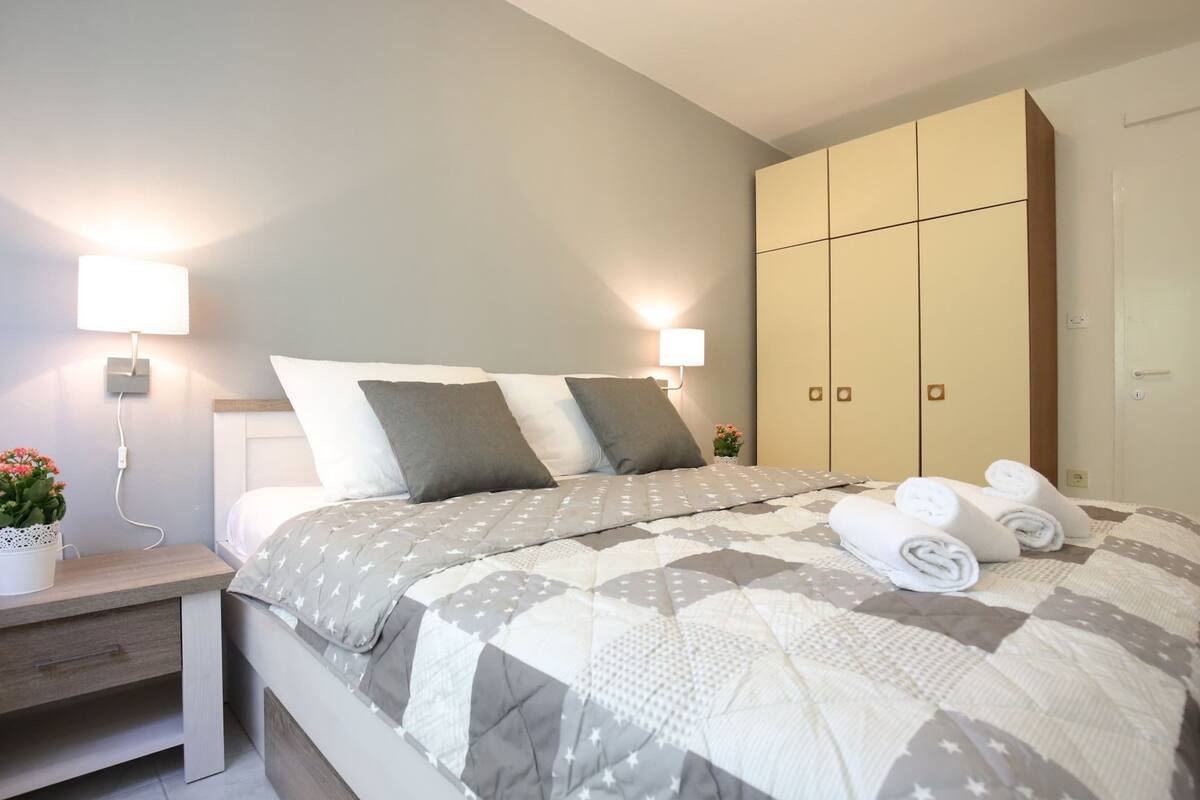 A neatly made bed with a quilt, bedside lamps, a nightstand with a plant, and a wardrobe.
