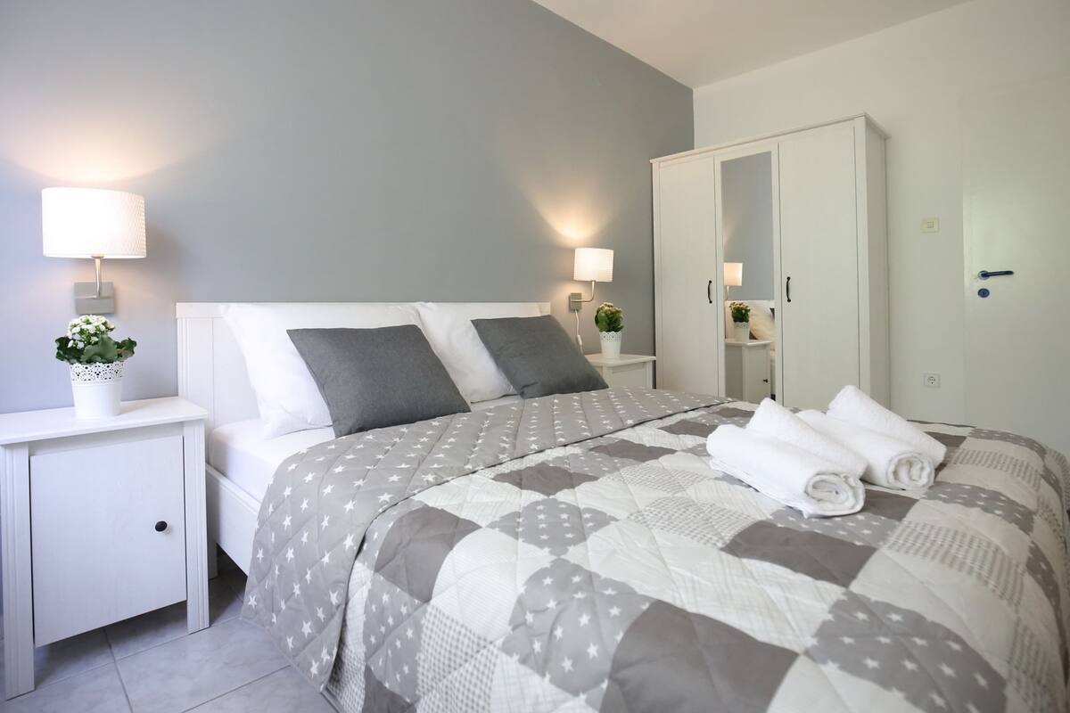 A neatly arranged bedroom with a bed, bedside tables, a wardrobe, and a mirror.
