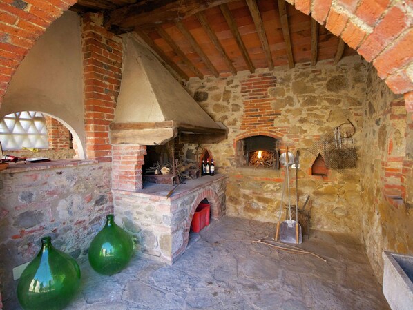 Ein rustikaler Steinraum mit Backofen, Kamin aus Stein und einem großen Bogenfenster.