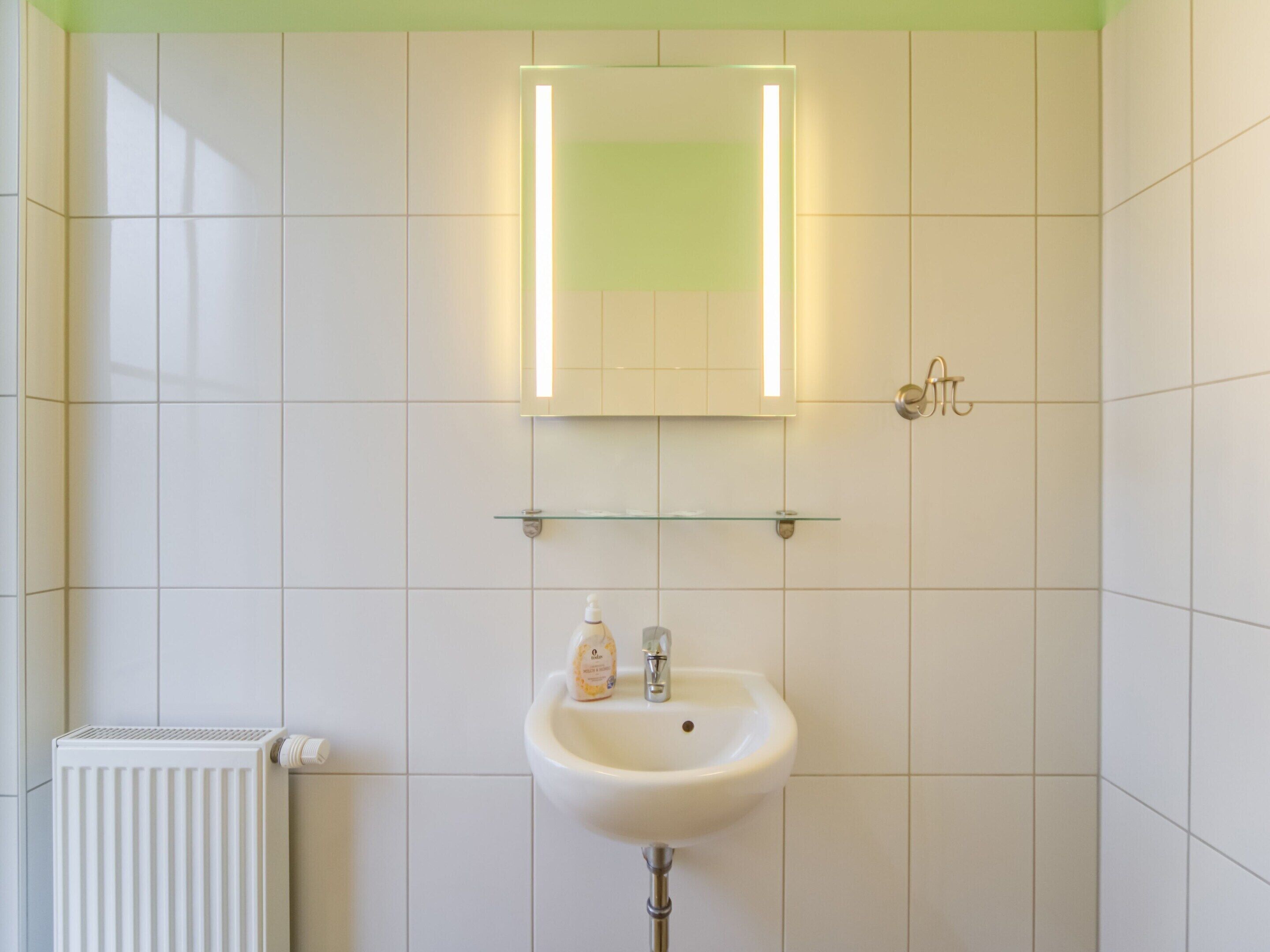 A bathroom with a white sink, a mirror with a light, and a radiator.