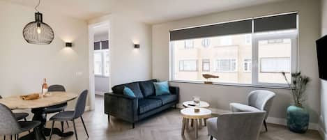 A modern living room with a dining area, a sofa, and a TV mounted on the wall.