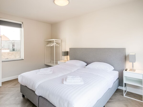 Quarto de hotel moderno com uma cama grande, uma mesa de cabeceira, um guarda-roupa e uma janela com vista para edifícios.