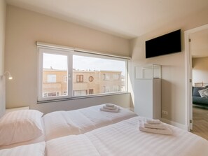 Quarto de hotel com cama, televisão fixada na parede e janela com vista para um edifício.