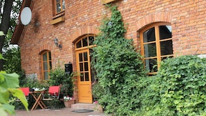 A brick building with a yellow door, arched windows, and a brick pathway leading to a table with chairs. - Mansion in Gressow With Terrace, Garden, Bbq, Pond, Bicycles (Gaegelow)