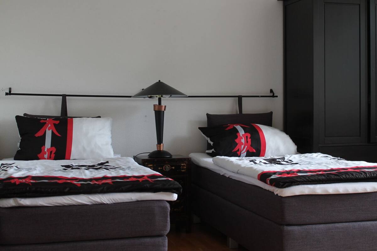 A bedroom with two beds, a nightstand, a lamp, and a wardrobe.