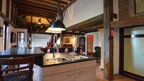 Une cuisine rustique avec des poutres apparentes, un grand îlot central doté d’un évier et un luminaire suspendu.
