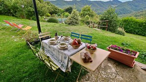 Un espace de restauration en plein air avec une table dressée pour deux personnes, entourée de chaises, d’un banc et d’un pot de fleurs.