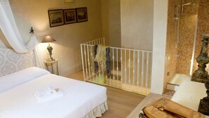 A hotel room with a bed, a small table with a lamp, a white railing, and a shower area.