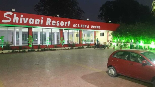 Resort Shivani con aire acondicionado y habitaciones NONA, zona de estacionamiento pavimentada y una motocicleta al fondo.