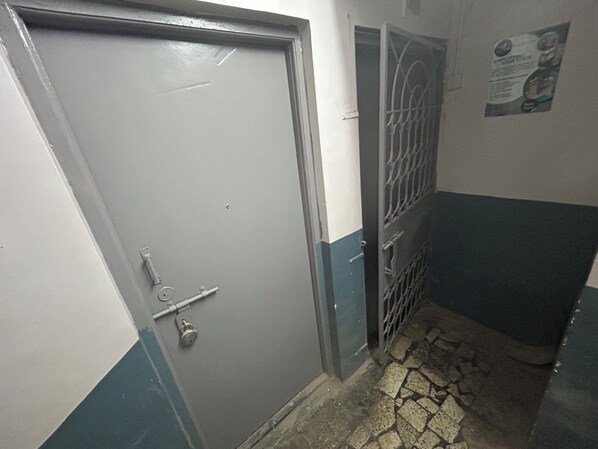 A narrow hallway with a door, a metal gate, and a tiled floor. - Solo Stays Pune (Pune)