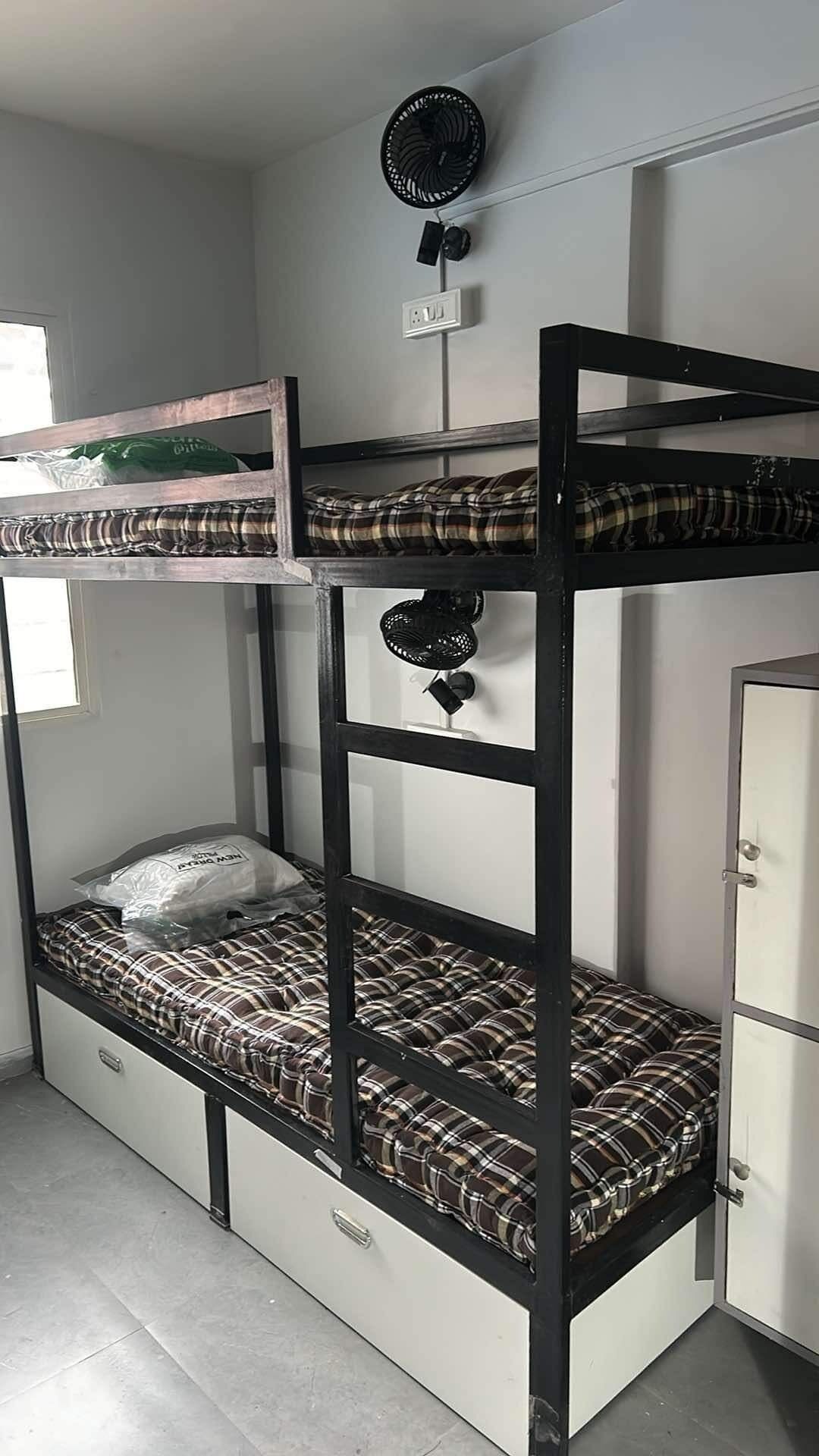 A bunk bed with a storage drawer underneath, a small fan on the top bunk, and a white cabinet to the right.