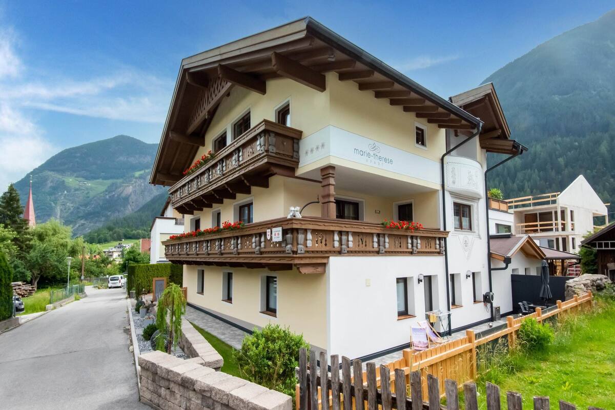 A multi-story building with a balcony, a sign reading "Marie Therese," and a mountainous backdrop.