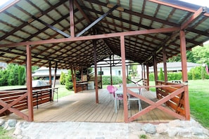 A covered outdoor seating area with tables and chairs, a wooden deck, and a stone border. - Holiday House in Szczecin at the Lake With Parking Space for 4 Persons (Szczecin)