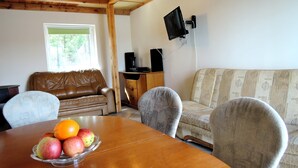 A dining area with a wooden table, chairs, a sofa, and a television mounted on the wall. - Holiday House in Szczecin at the Lake With Parking Space for 4 Persons (Szczecin)