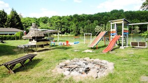 A playground with slides and swings, a picnic table, and a fire pit. - Holiday House in Szczecin at the Lake With Parking Space for 4 Persons (Szczecin)