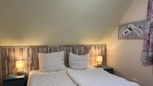 A bedroom with a wooden headboard, two bedside tables with lamps, a large bed with white bedding, and a wall-mounted artwork.