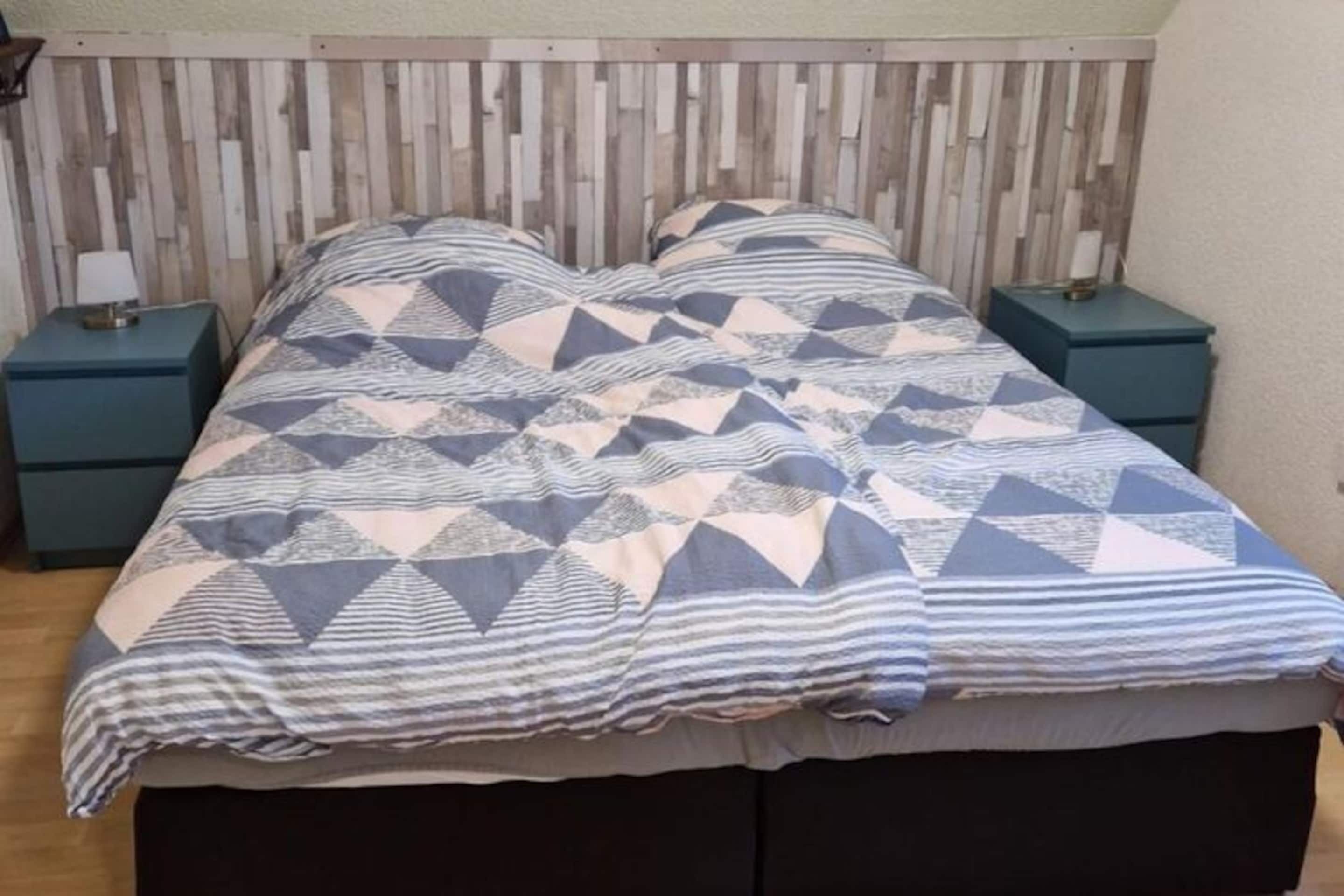 Een bed met een bedspreider met geometrisch patroon, twee nachtkastjes en een houten hoofdbord.