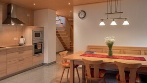 Una cocina moderna con armarios de madera, horno empotrado y comedor con mesa y sillas de madera.