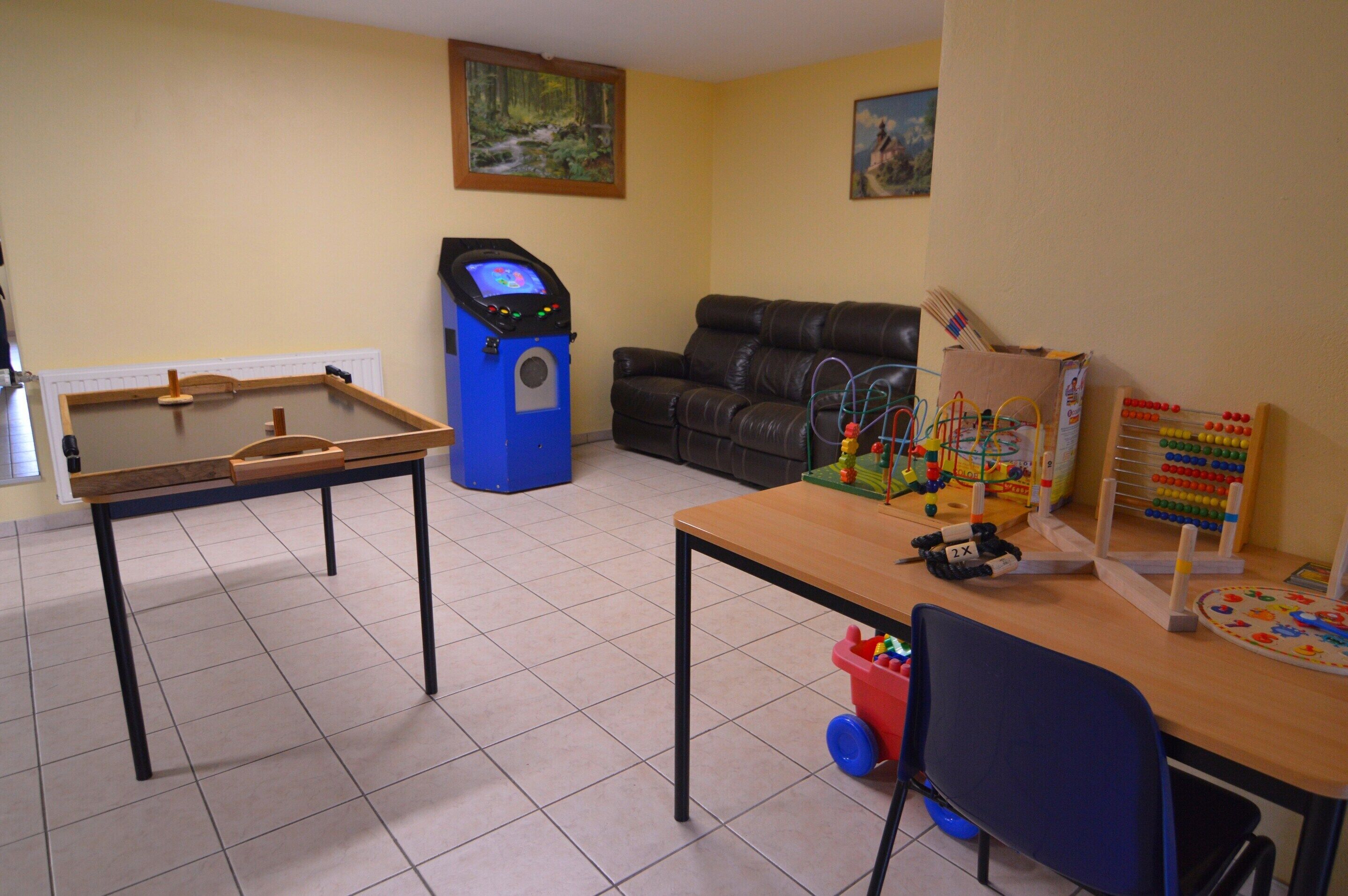 Um quarto com mesa de pebolim, máquina de jogos eletrônicos azul, sofá e brinquedos educativos sobre uma mesa.