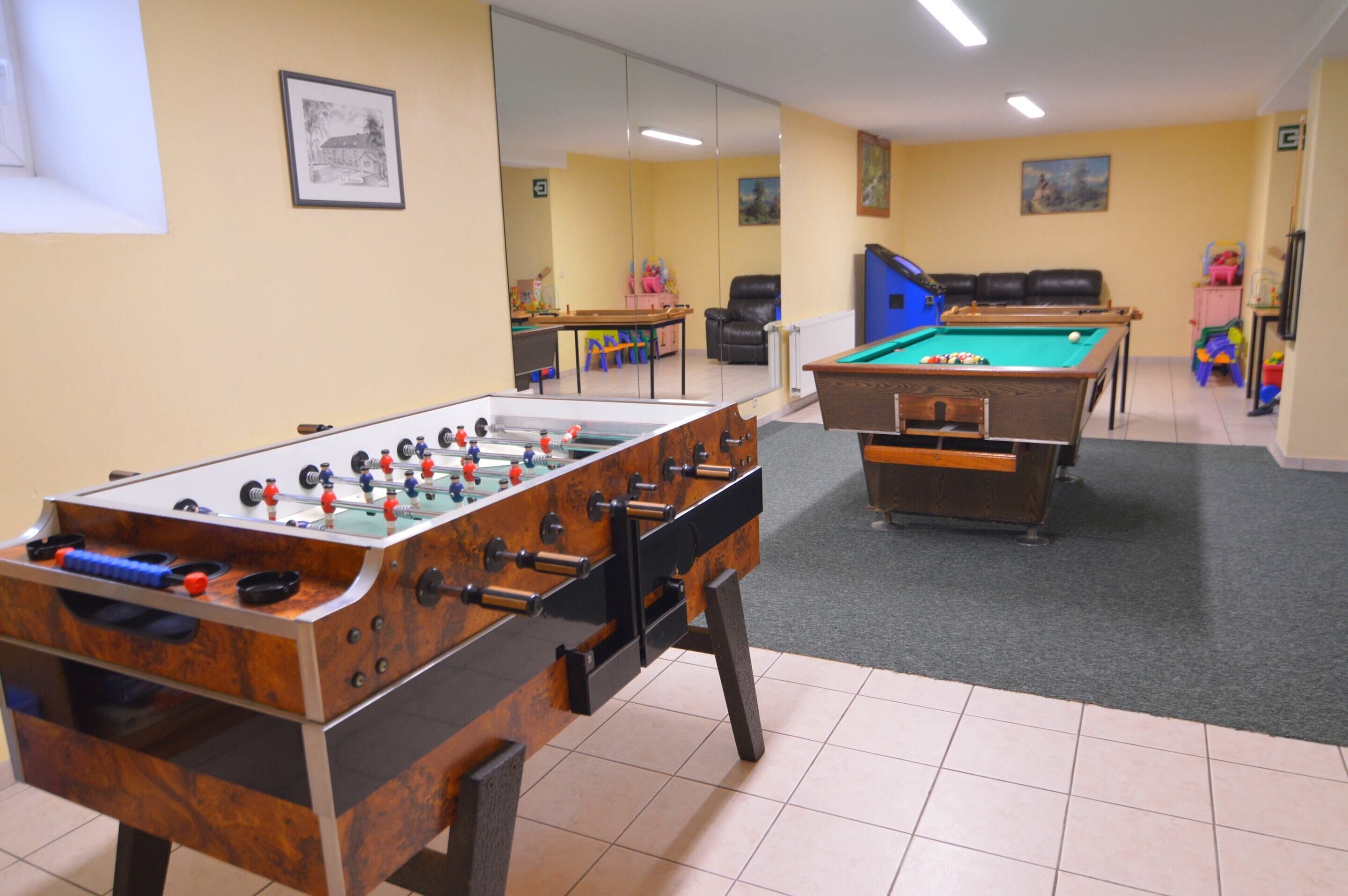 Um espaço com duas mesas de pebolim, uma mesa de bilhar e uma mesa de sinuca.