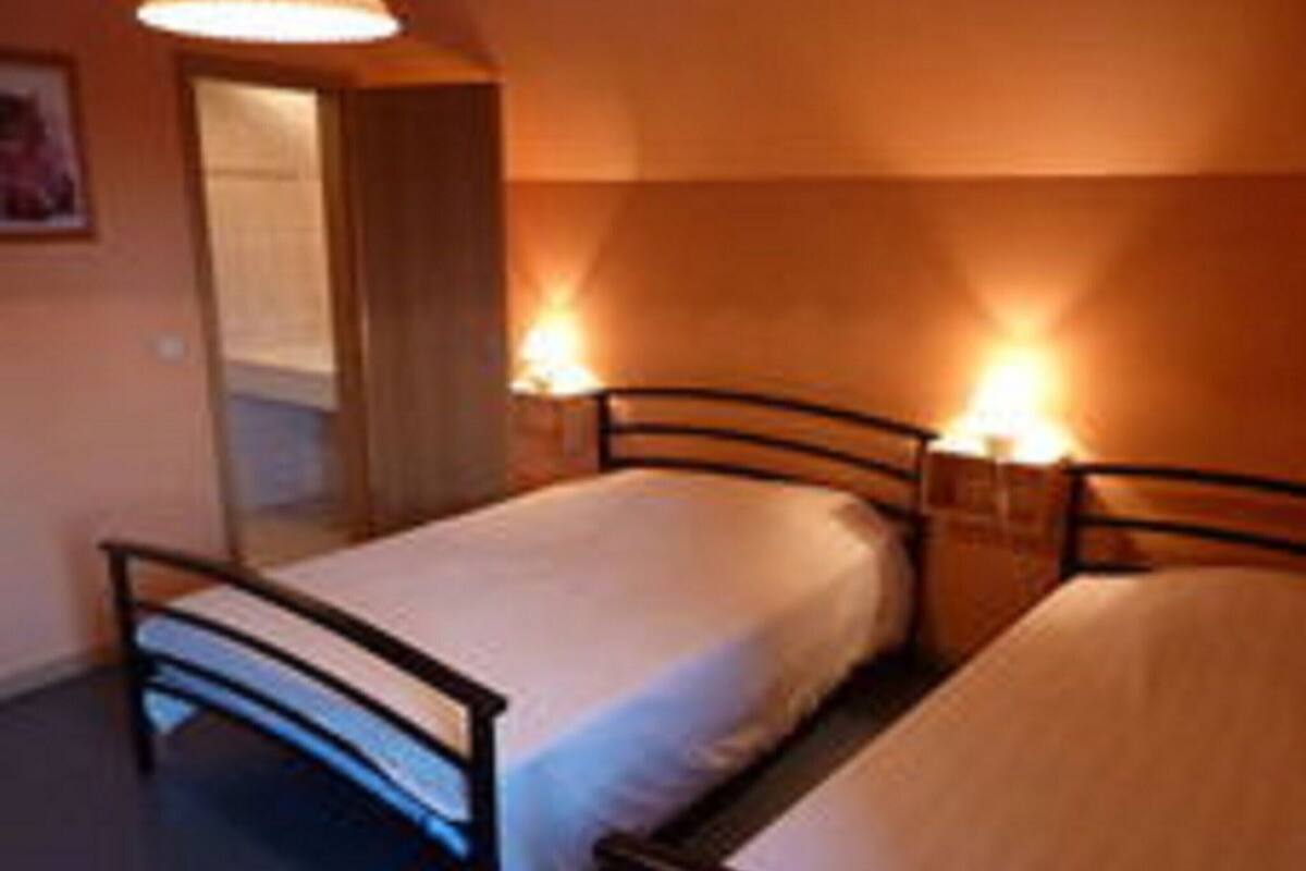Een kleine, gezellige kamer met twee enkele bedden, een houten deur en een lamp aan de muur.